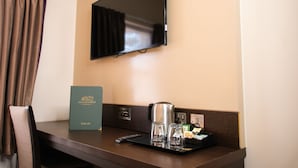 Ein Hotelzimmer mit Flachbildfernseher an der Wand, einer Kaffeemaschine, einer Weinkarte und einer Fernbedienung auf einem Tablett.