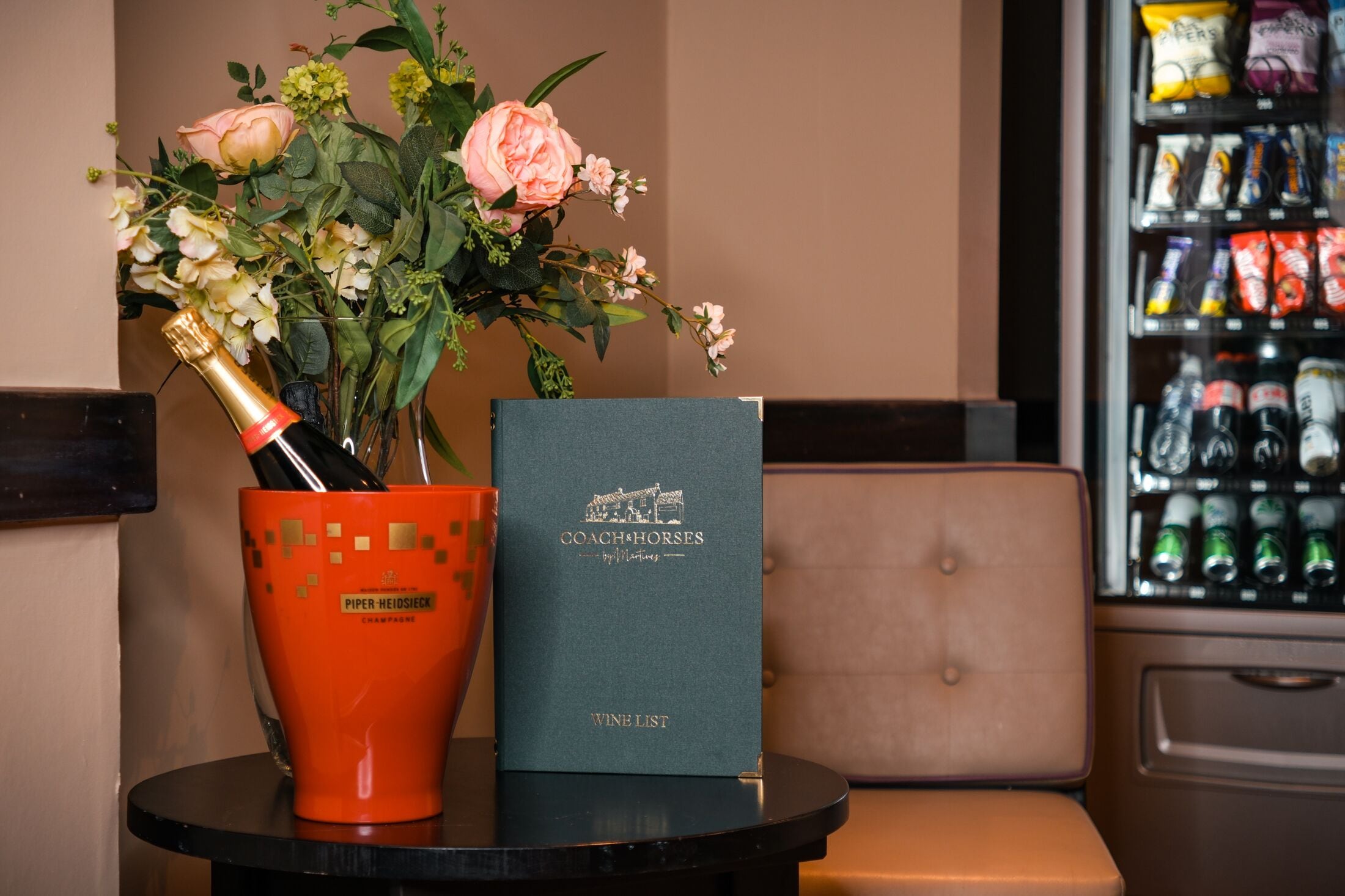 A table with a bottle of champagne, a bouquet of flowers, and a wine list book.