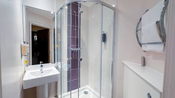 Un baño moderno con ducha de vidrio, lavamanos blanco y perchero para toallas.