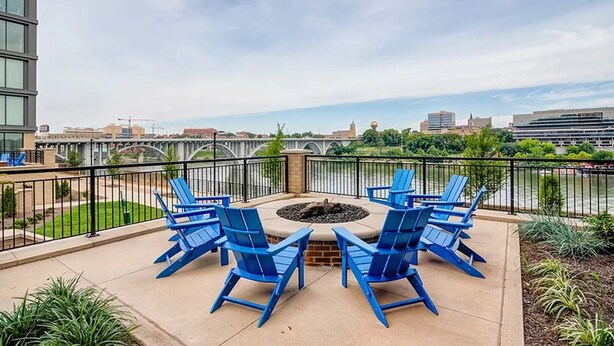 A patio with blue Adirondack chairs and a fire pit, overlooking a river and cityscape. - Landing | Chic 1BD, Clubhouse, Gym (Knoxville)