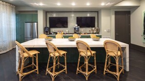 A modern kitchen with a large island, green cabinets, and wicker chairs.