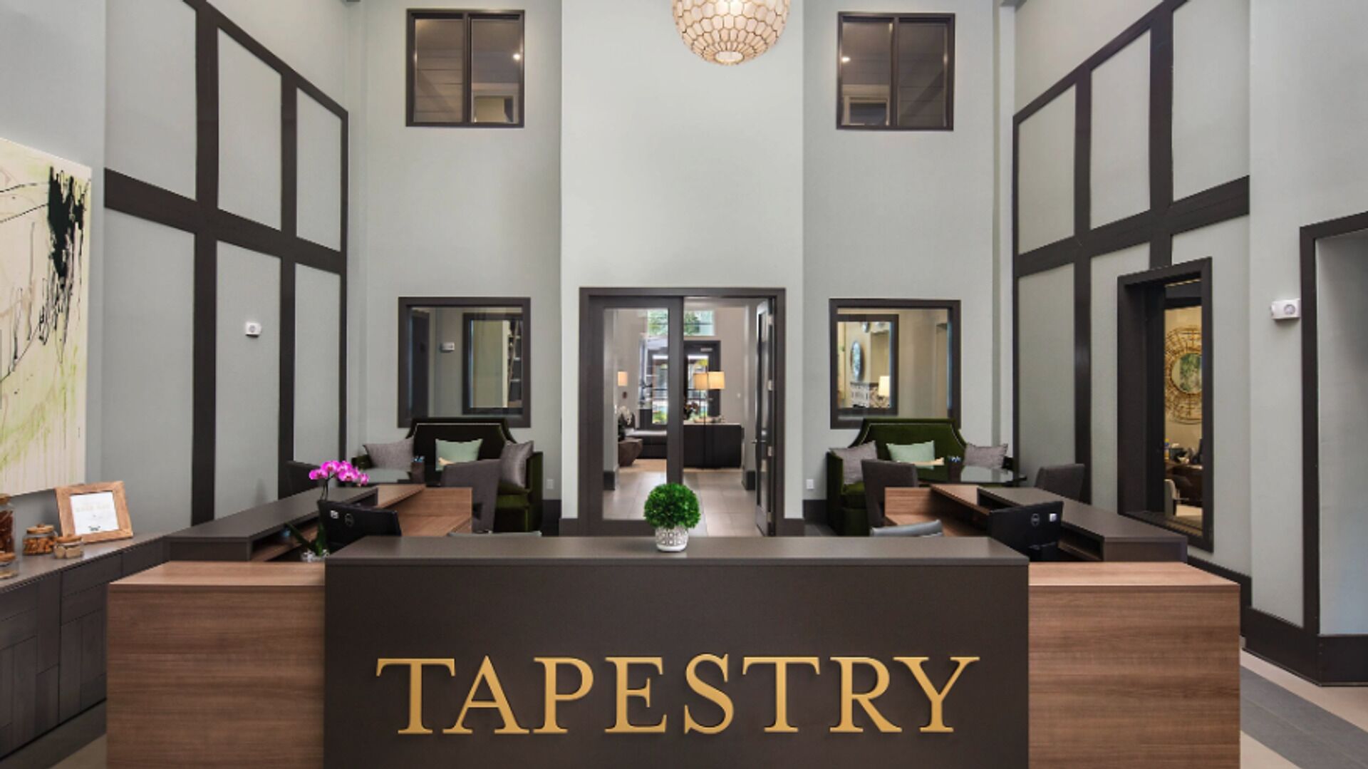 Vastaanottotiski, jossa on kultaisin kirjaimin kirjoitettu sana ”TAPESTRY”, ja sen molemmin puolin kaksi oleskelualuetta, joissa on sohvia ja nojatuoleja, sekä keskellä suuri kasvi.