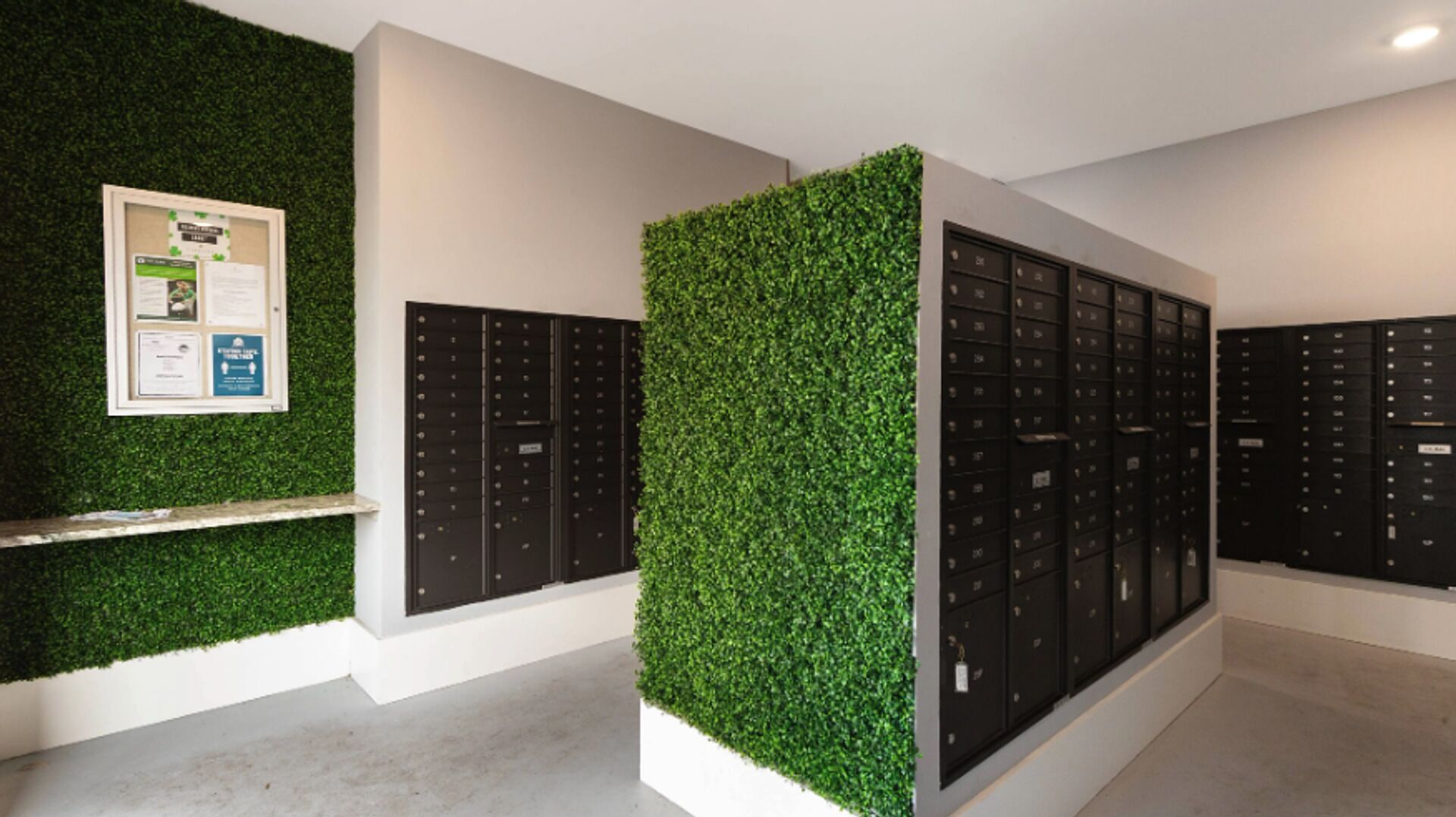 Een moderne lobby met een groene wand, een prikbord en rijen zwarte lockers.