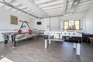 Une pièce avec deux tables de baby-foot, une fenêtre donnant sur un beau paysage et un téléviseur fixé au mur.