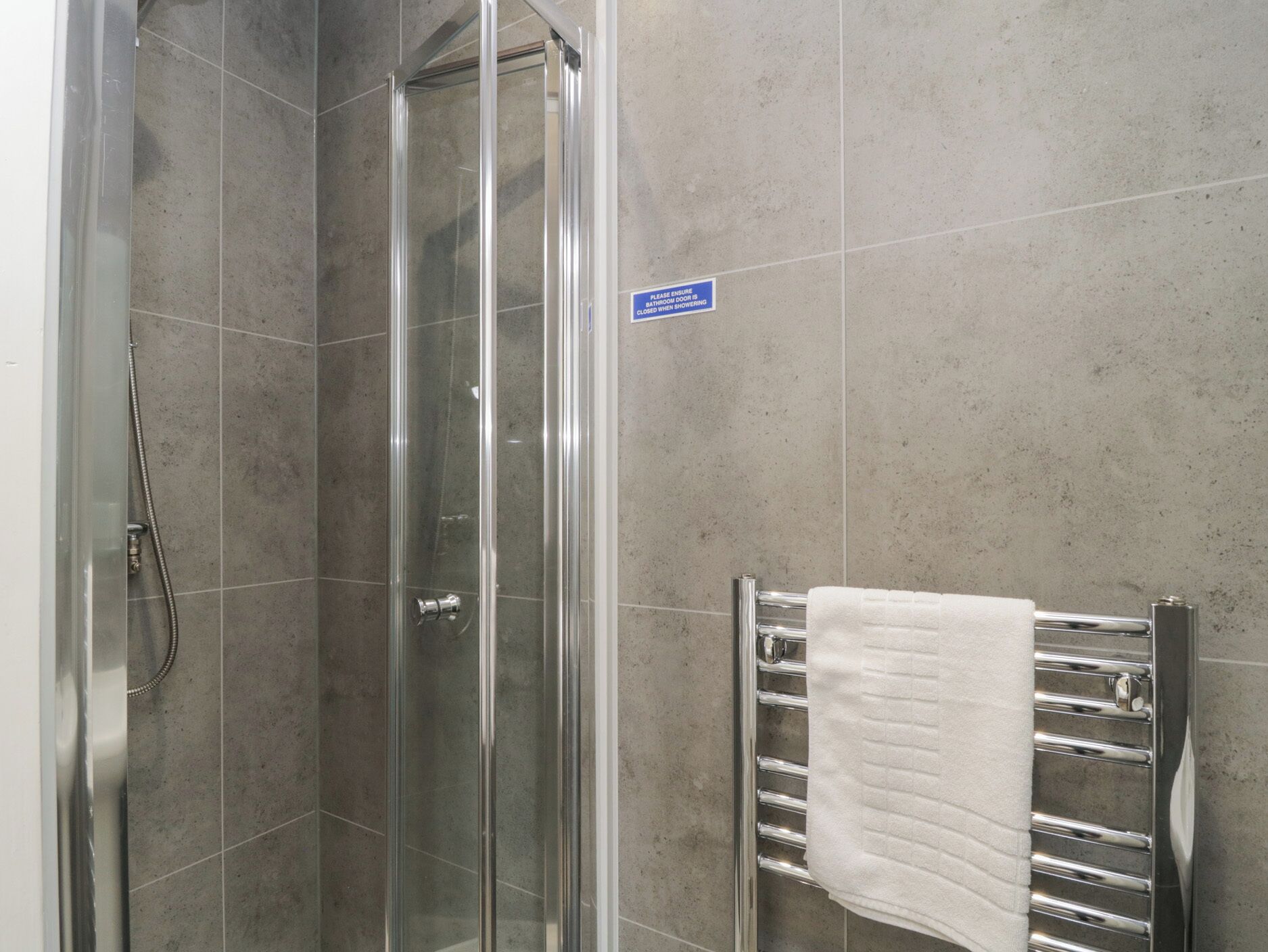 A glass-enclosed shower with a towel rack beside it.