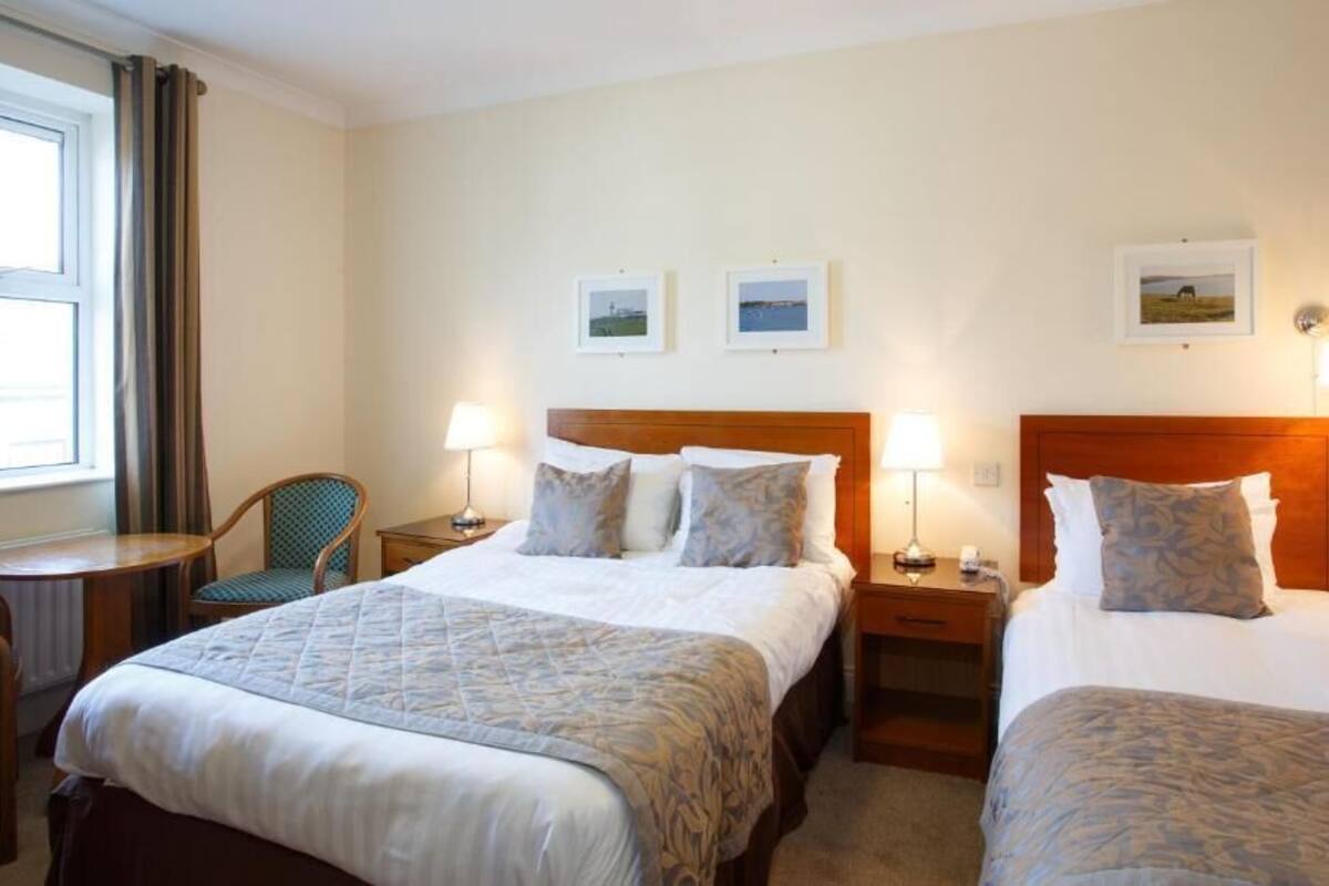 A hotel room with two beds, a chair, a small table, and a window with curtains.