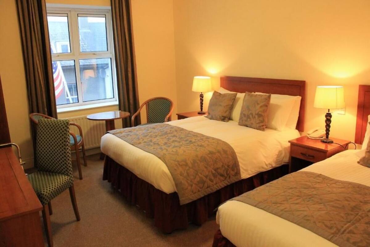 A hotel room with two beds, a chair, a table, and a window with curtains.