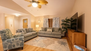 A living room with a sofa, armchair, TV, and a ceiling fan.