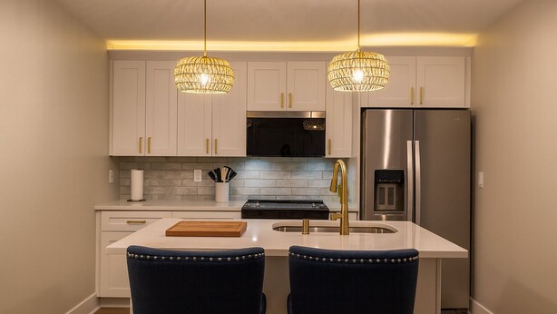 A modern kitchen with white cabinets, a stainless steel refrigerator, a built-in oven, and two pendant lights.