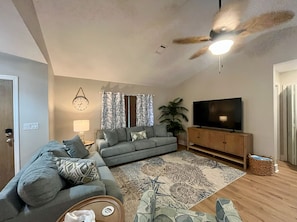 Relax in this inviting living room with a large flat-screen TV, comfortable sofa, and a potted plant.