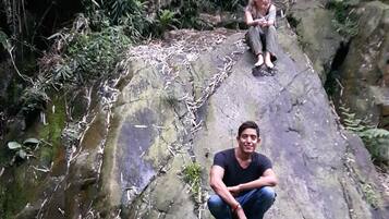 Two people sitting on a rocky surface in a natural setting with dense foliage in the background.