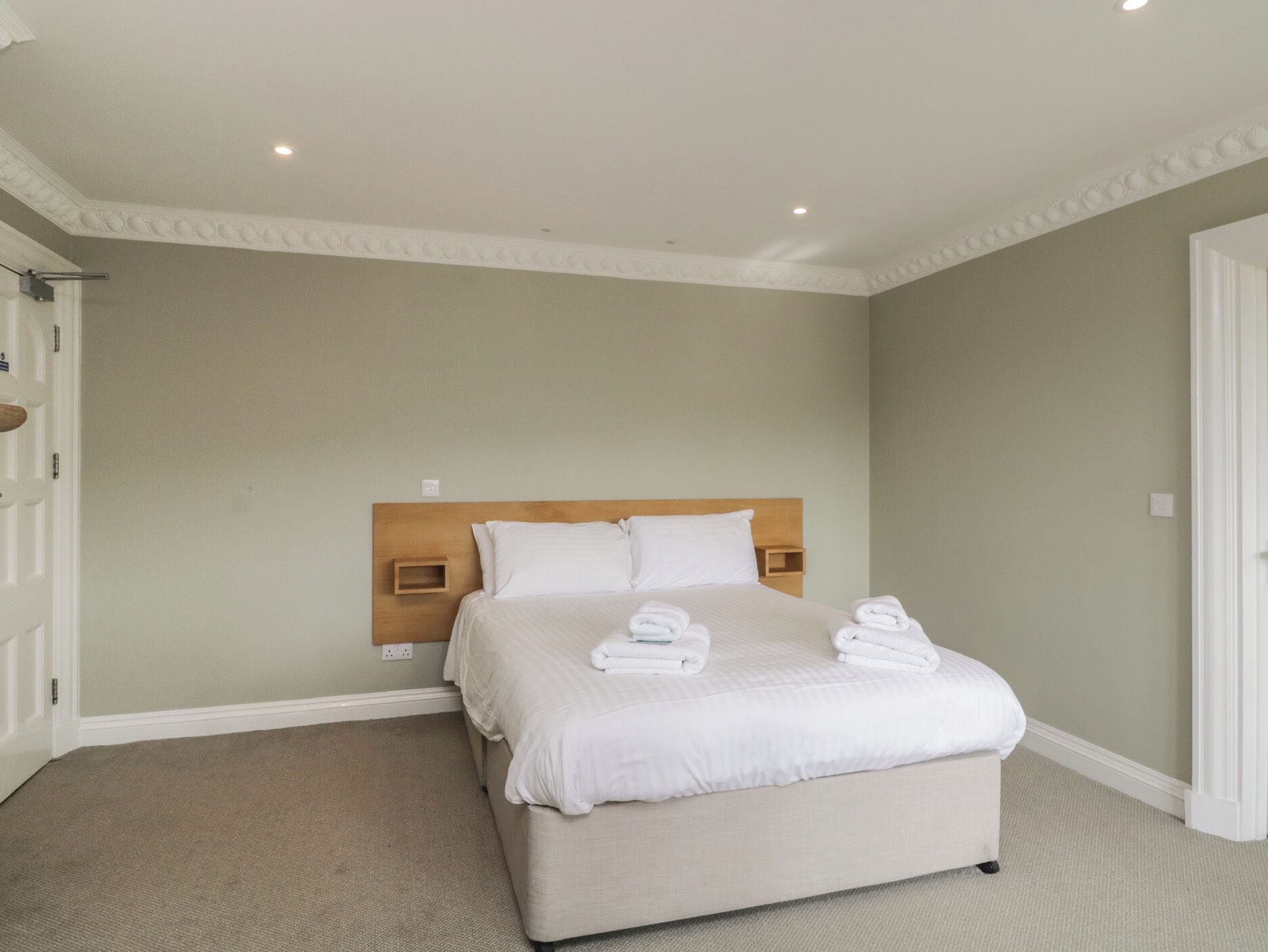 Una camera da letto ordinata con un grande letto, una testiera in legno e un pavimento coperto da moquette.