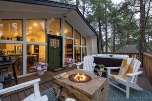 Une terrasse extérieure accueillante, dotée d’un foyer, de chaises Adirondack blanches et d’un bain à remous.
