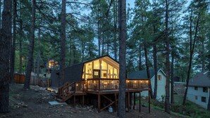 Eine Holzhütte mit einer Holzterrasse und einer Glasfront, umgeben von hohen Kiefern.