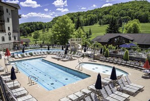 Zona de piscina con sillas de descanso, tobogán y vista a un paisaje verde.