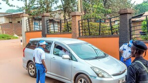 A silver car parked in front of a gated entrance with a stone pillar and metal gate. - Jevine Hotel (Kampala)