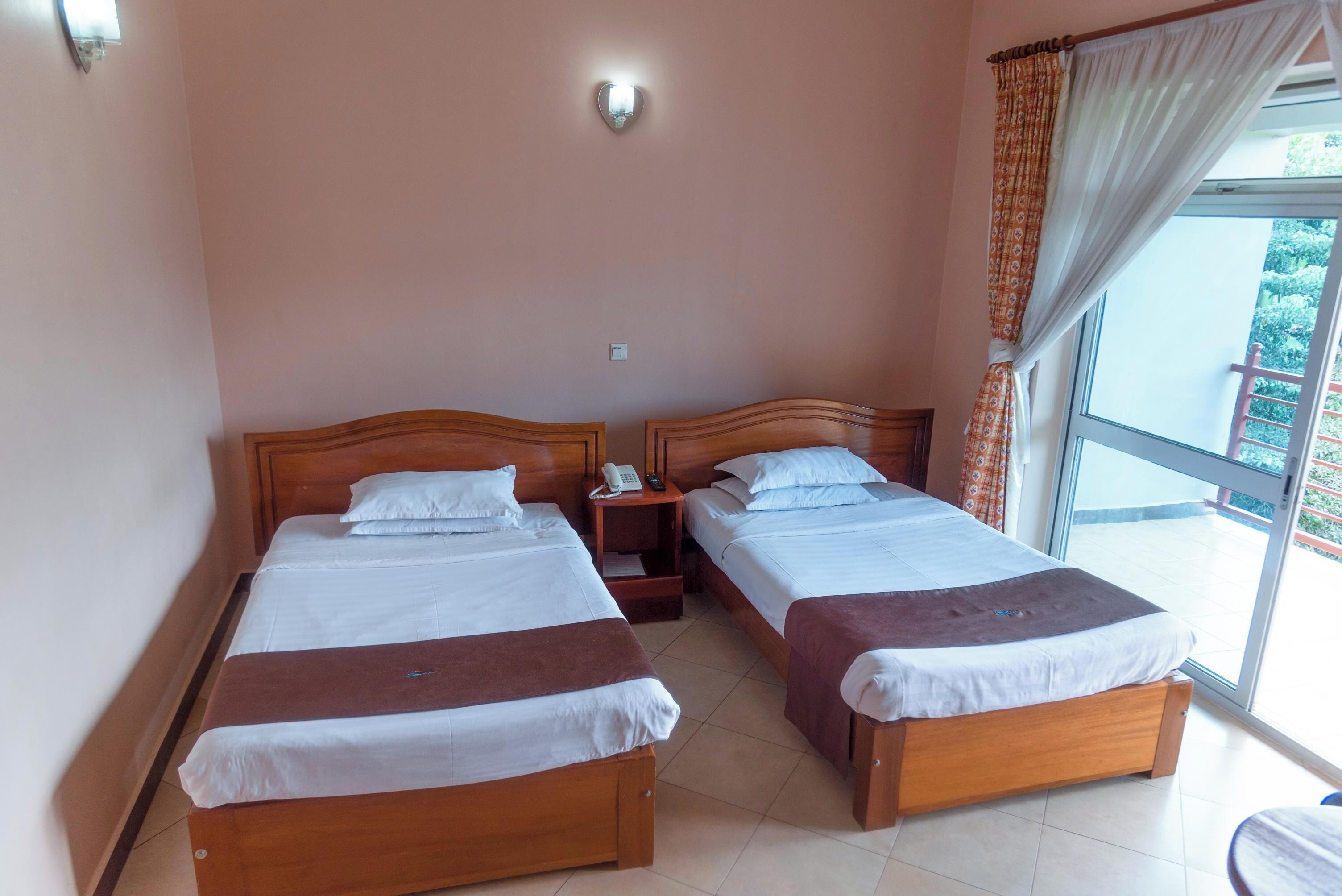 Una habitación de hotel con dos camas de madera, una mesita de noche con teléfono y una ventana con cortinas.