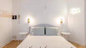 A bedroom with a bed, two bedside tables, a wall-mounted light fixture, and a neon sign.