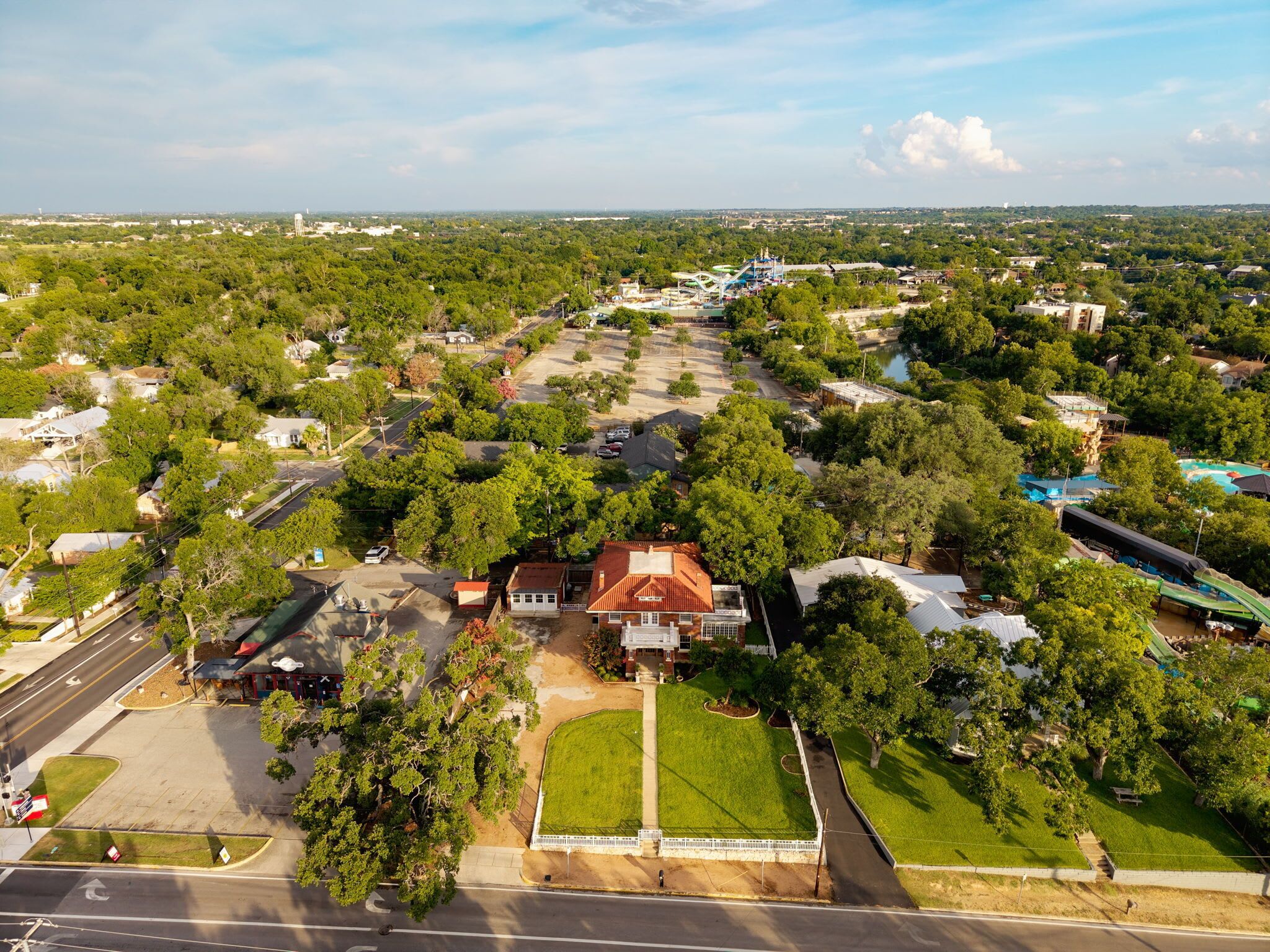 An aerial view of a residential area with houses, a large green field, and a parking lot.