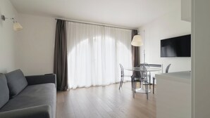 Een moderne woonkamer met een grijze bank, een eethoek met een tafel en stoelen, en een groot raam met gordijnen.