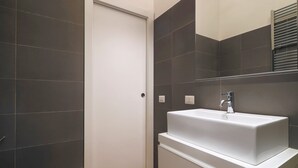 Een moderne badkamer met donkere tegels, een witte wastafel en een deur.