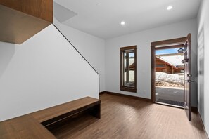 A modern interior with a wooden staircase, a bench, and a view of a snowy landscape through a glass door.