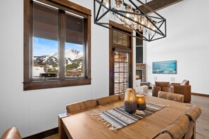 Un espace repas comprenant une table en bois, des chaises en cuir, une vue sur les montagnes et un lustre moderne.