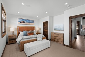 A bedroom with a bed, bedside tables, a bench, a dresser, and a painting on the wall.