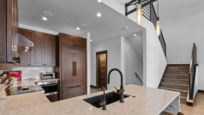 A modern kitchen with a central island, built-in appliances, and a staircase leading to an upper level.