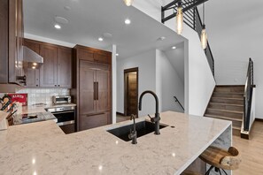 Une cuisine moderne dotée d’un îlot central, d’appareils électroménagers intégrés et d’un escalier menant à un niveau supérieur.