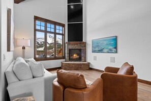 A cozy living room with a fireplace, a large window with a mountain view, and a painting on the wall. - *NEW TO MARKET* Mountain Chalet | 2 Min from Big Sky Resort | Hot Tub (Big Sky)