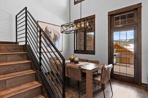 A wooden staircase with a black railing leading to a dining area with a table and chairs. - *NEW TO MARKET* Mountain Chalet | 2 Min from Big Sky Resort | Hot Tub (Big Sky)
