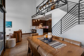 A modern interior with a dining area, leather seating, a staircase with glass jars, and a kitchen in the background.