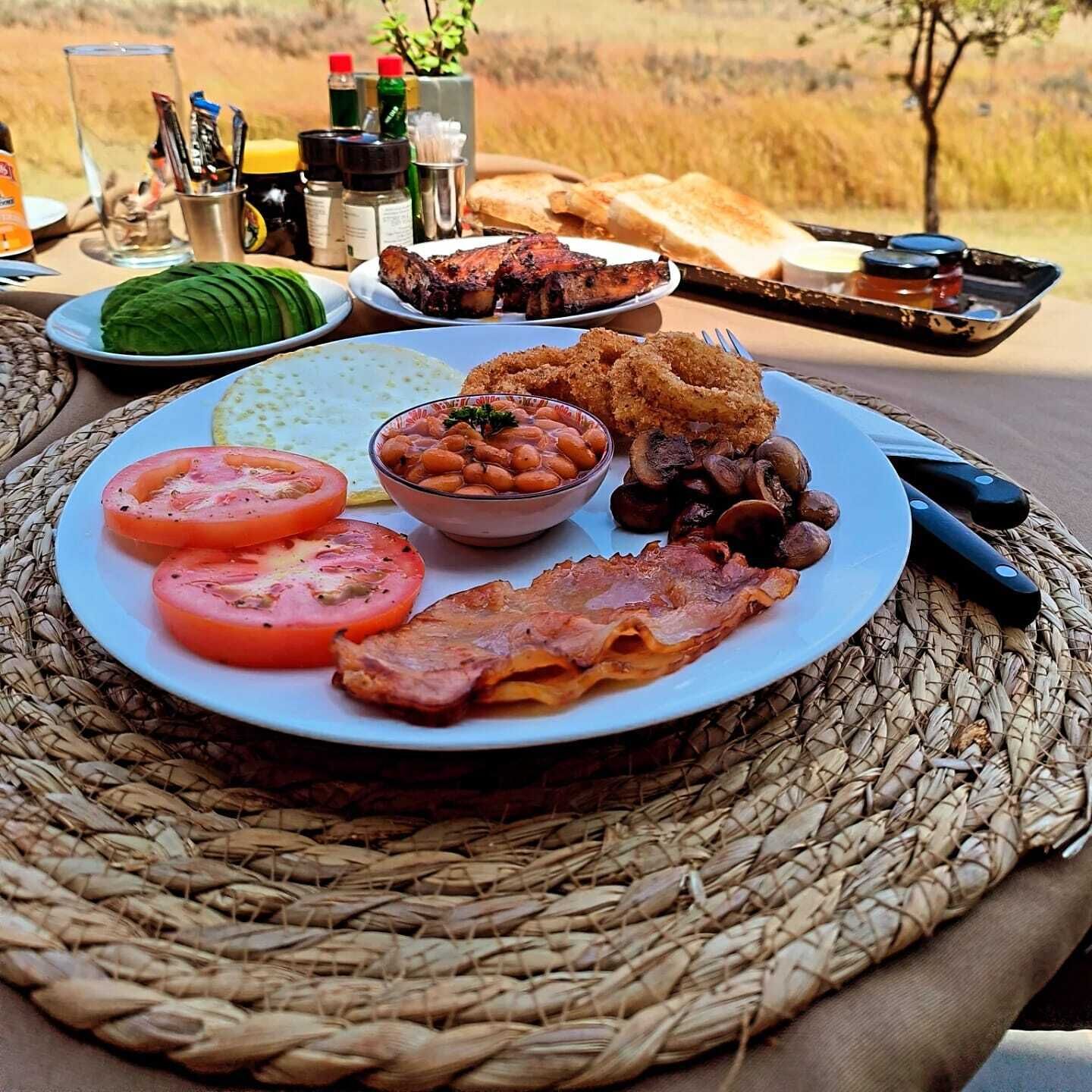 A breakfast plate with bacon, tomatoes, beans, and toast on a woven mat.