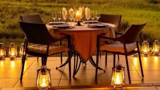 An outdoor dining setup with a table and chairs, surrounded by lanterns, set against a backdrop of a mountainous landscape during sunset. - Sofala Lodge (Sterkrivier)