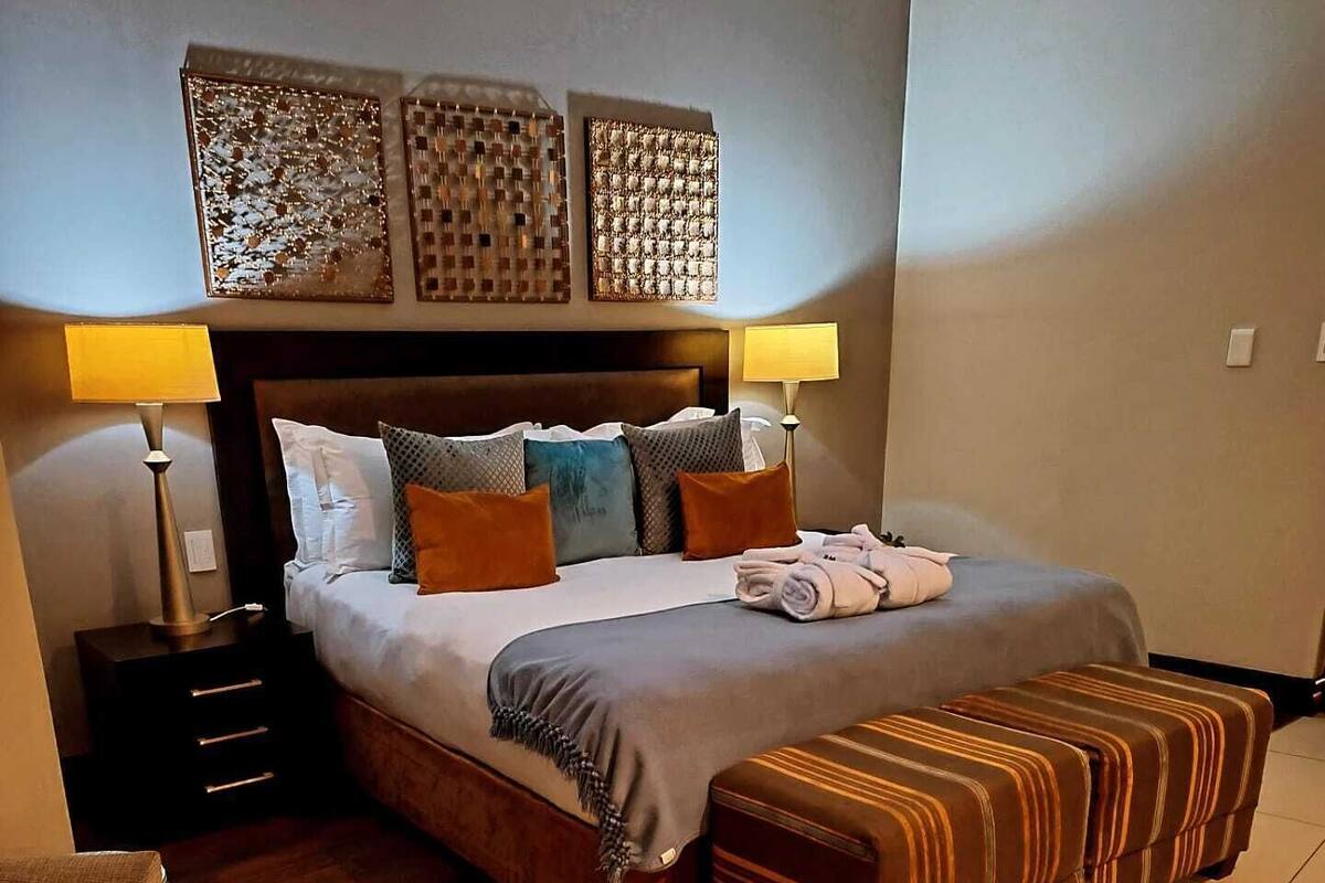 A neatly arranged hotel room with a large bed, two bedside tables, a bench, and decorative wall art.
