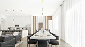 A modern dining area with a long table set for a meal, surrounded by sofas and chairs. - Avatar Gameroom/Theater/Resort Access/Huge 15BR! (Kissimmee)