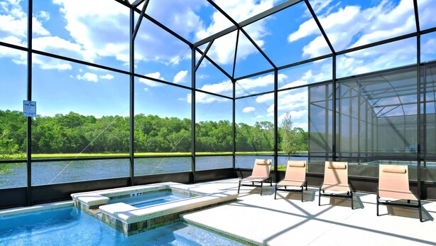 A glass-enclosed swimming pool with lounge chairs and a view of a lake and forest. - Avatar Gameroom/Theater/Resort Access/Huge 15BR! (Kissimmee)