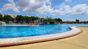 A large outdoor swimming pool with a water slide, surrounded by lounge chairs and umbrellas. - Tucano Apartment Club Resort (Isola di Capo Rizzuto)