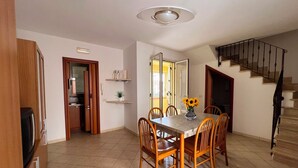 A dining area with a table, chairs, and a vase of sunflowers. There is a staircase to the right and a door leading to another room. - Tucano Apartment Club Resort (Isola di Capo Rizzuto)