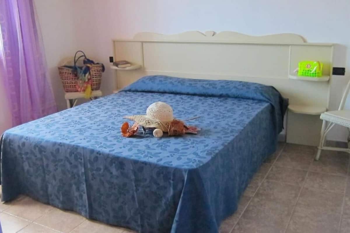 A bedroom with a bed covered in a blue floral bedspread, a wicker basket, and a small chair.
