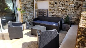 An outdoor seating area with wicker furniture, a stone wall, and a sliding glass door.