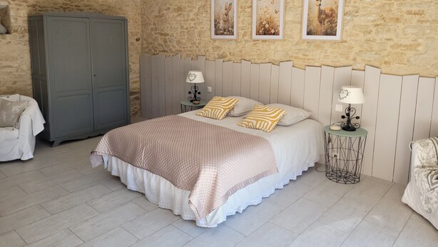 A bedroom with a stone wall, a bed with a white headboard, two bedside tables with lamps, and a wardrobe.
