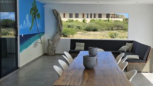 Een moderne eetruimte met een houten tafel, witte stoelen en uitzicht op een gebouw door grote ramen.