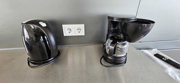 Two coffee makers on a stainless steel countertop with a power outlet in the background.