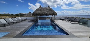 A pool area with lounge chairs and thatched umbrellas, overlooking a body of water.