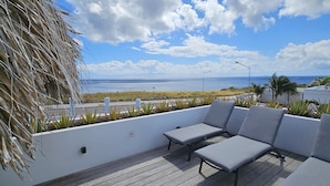 Een balkon met grijze zittingen, een witte balustrade en uitzicht op de oceaan.