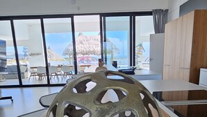 Een moderne kamer met een grote houten tafel, een decoratieve metalen sculptuur en uitzicht op de oceaan door grote ramen.