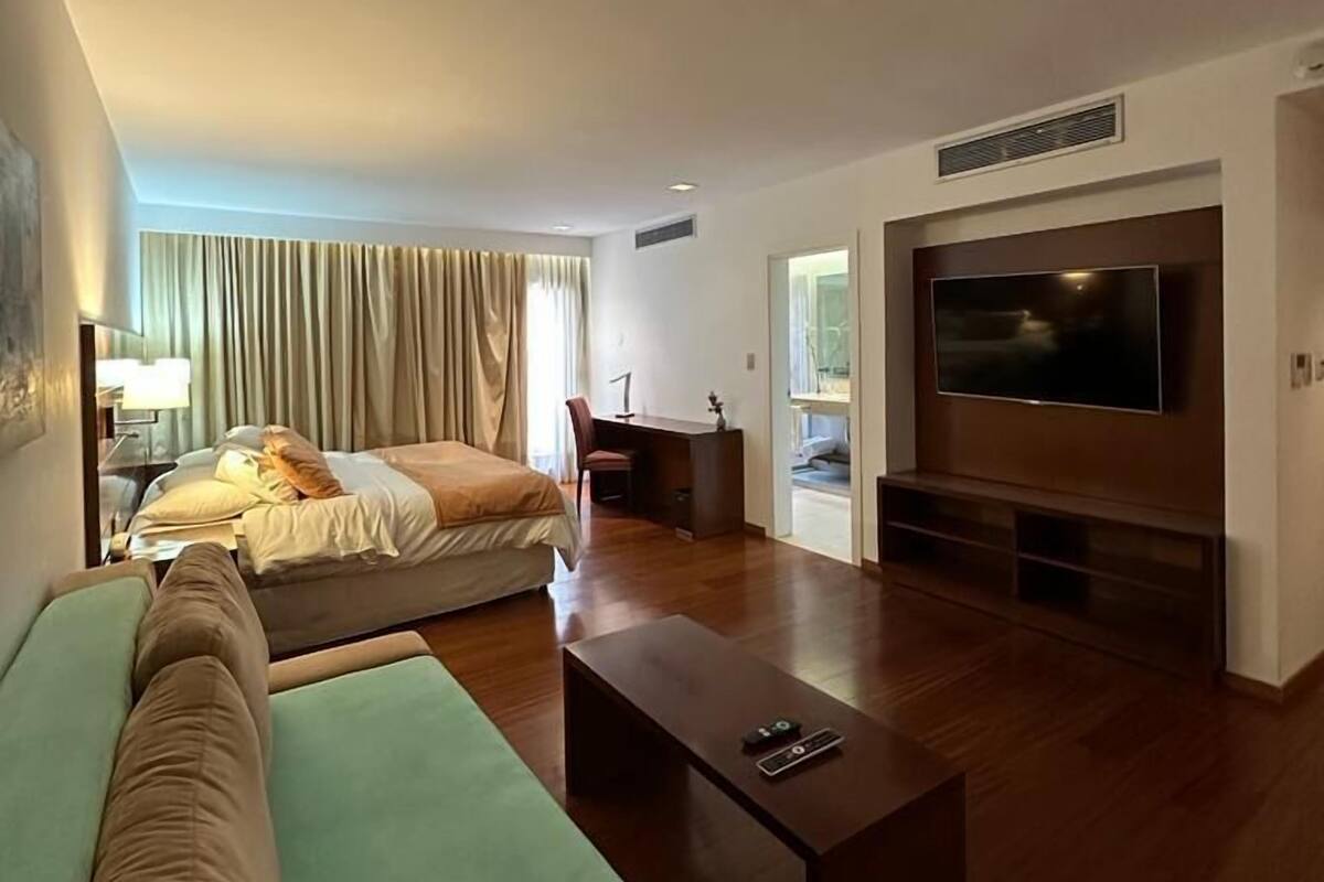 A modern hotel room with a large bed, a sofa, a TV, and a desk.