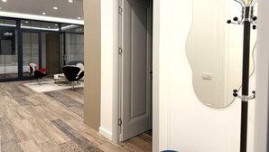 A modern room with a large mirror, a door leading to another room, and a seating area with chairs.